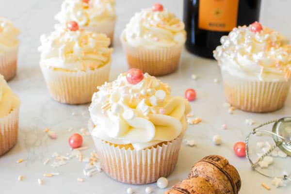 Prosecco cupcakes with buttercream on a table with sprinkles.