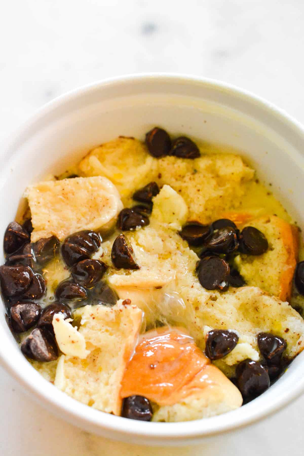 Close up of bread pudding with chocolate chips being made in a white bowl.