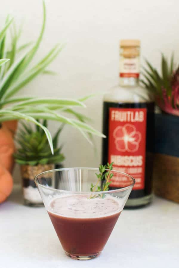 Stemless martini glass with a refreshing Hibiscus Martini Vodka Cocktail on a table next to Fruitlab Hibiscus Liqueur.