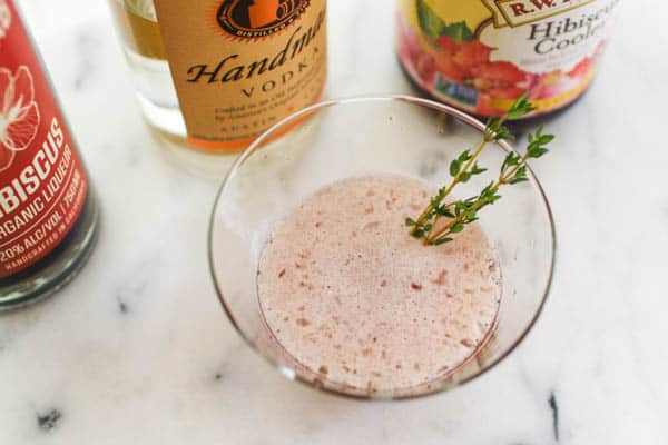 hibiscus martini on a counter with a sprig of thyme