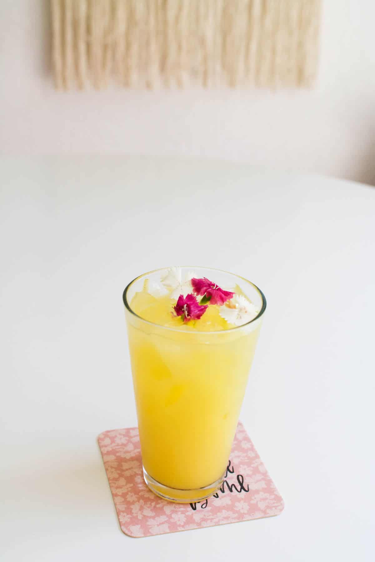 A tall glass with an orange juice cocktail on a table granished with pink flowers.