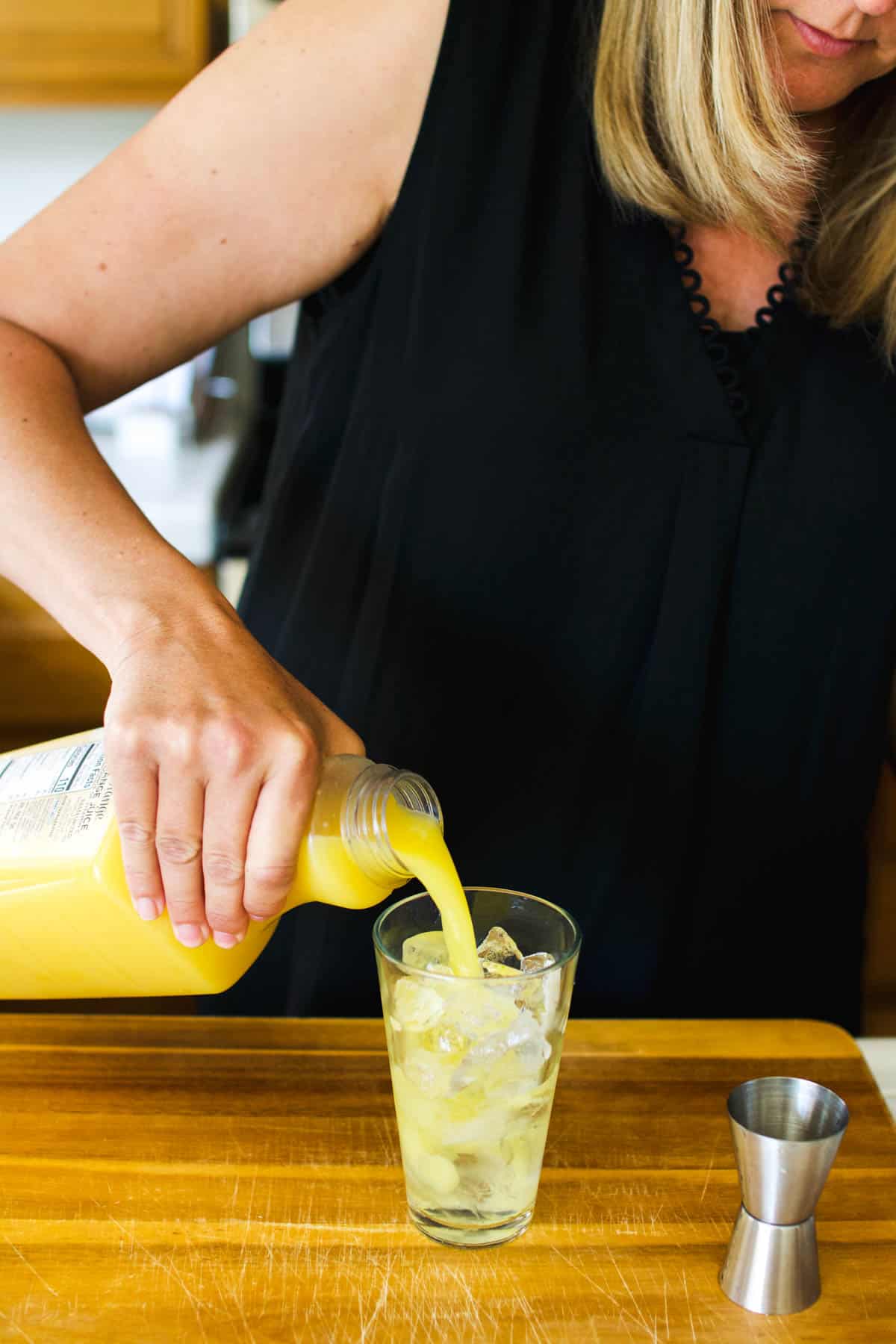 Woman pouring orange juice into a glass full of ice and vodka.