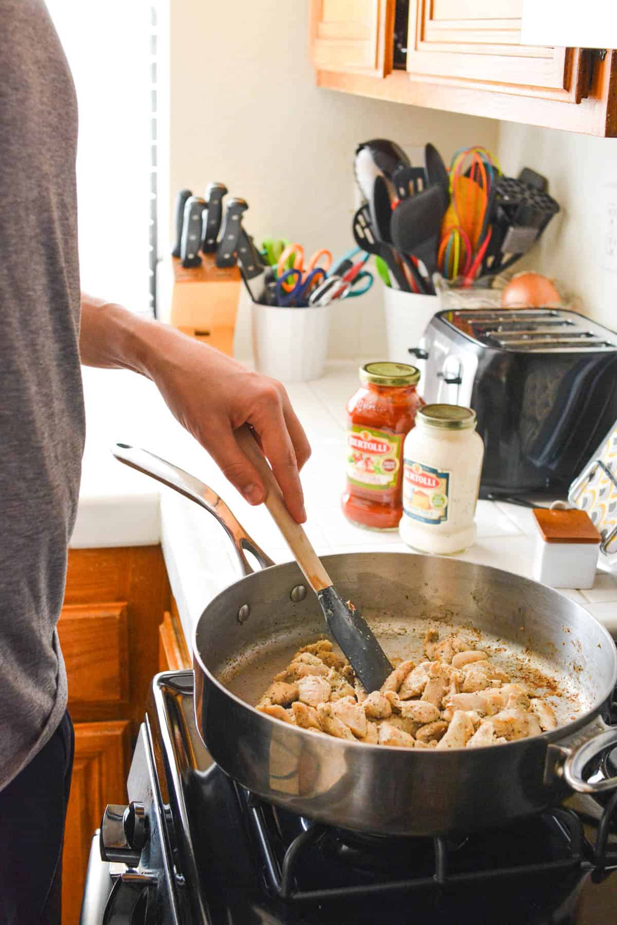 Man cooking chicken in a saute pan at the stove.