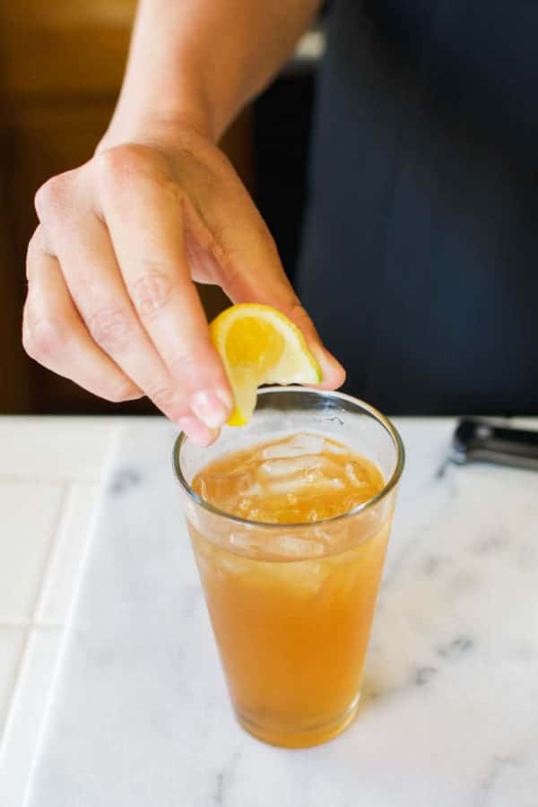 Woman squeezing a lemon wedge into a glass of iced tea.