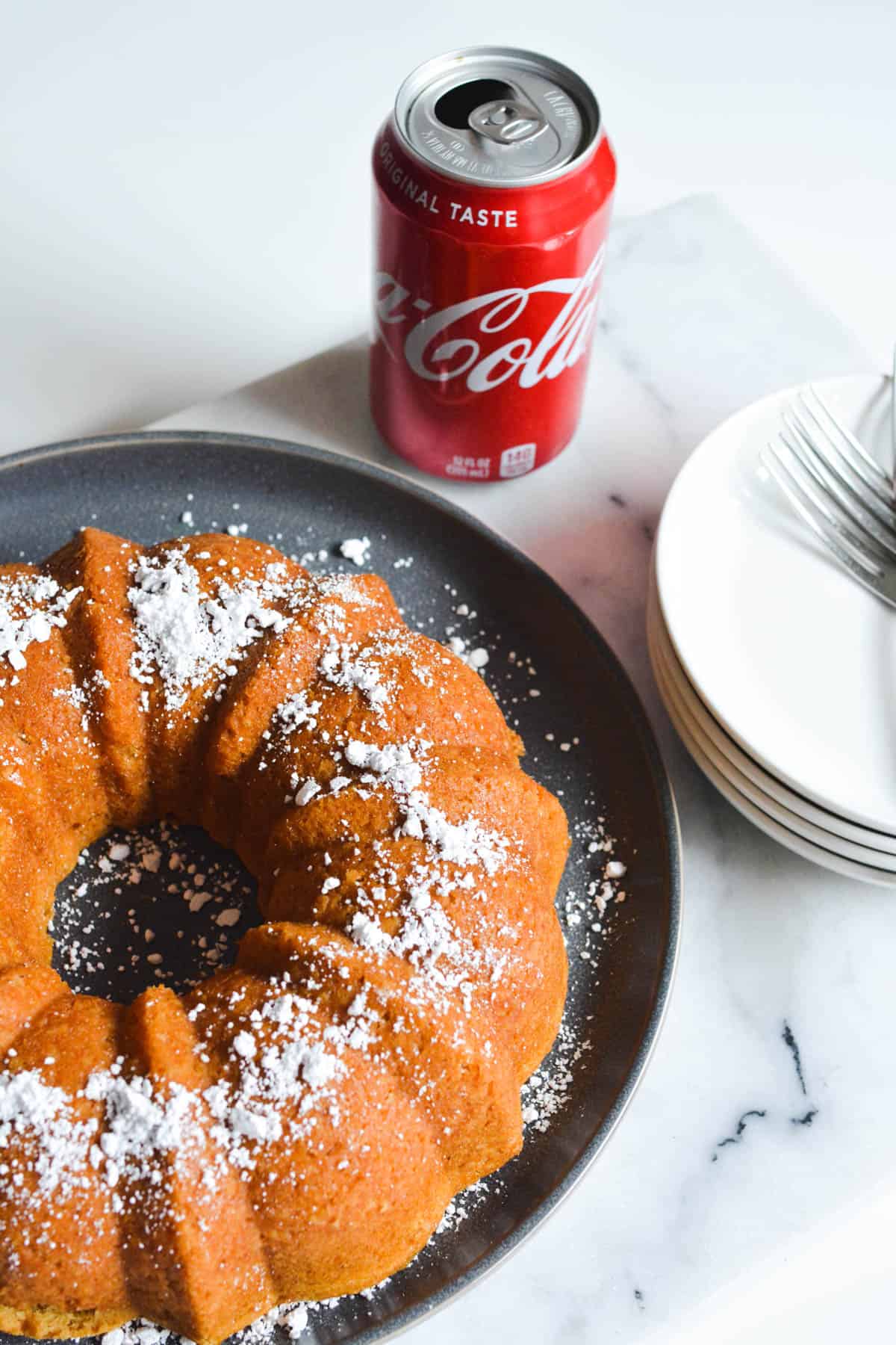 A bundt cake on a black plate on a table next to a can of Coke.