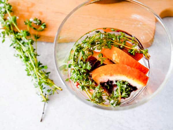 Pieces of blood orange and thyme in a glass next to a cutting board.