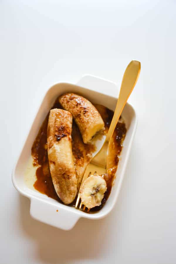 Baking dish of oven roasted bananas with butter and brown sugar with a fork.