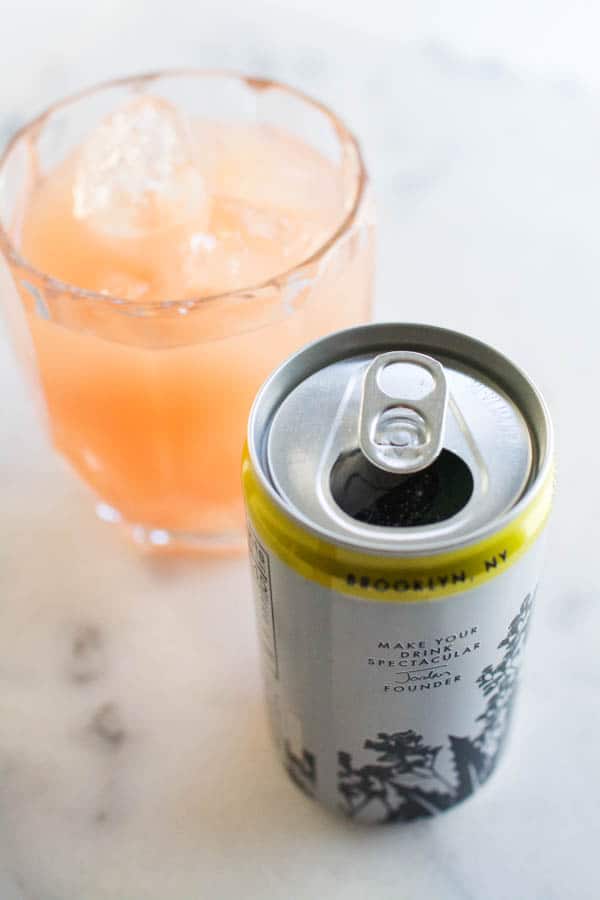 A close up of a glass of grapefruit juice next to a can of tonic.