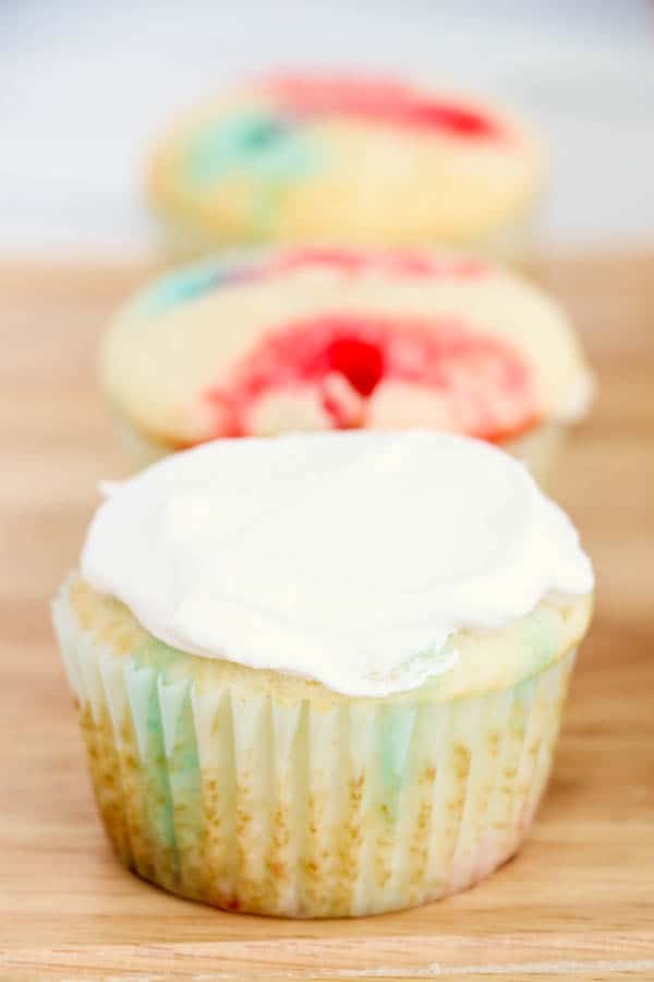 Easy jello poke cupcakes sitting on a table with one frosted with whipped cream.