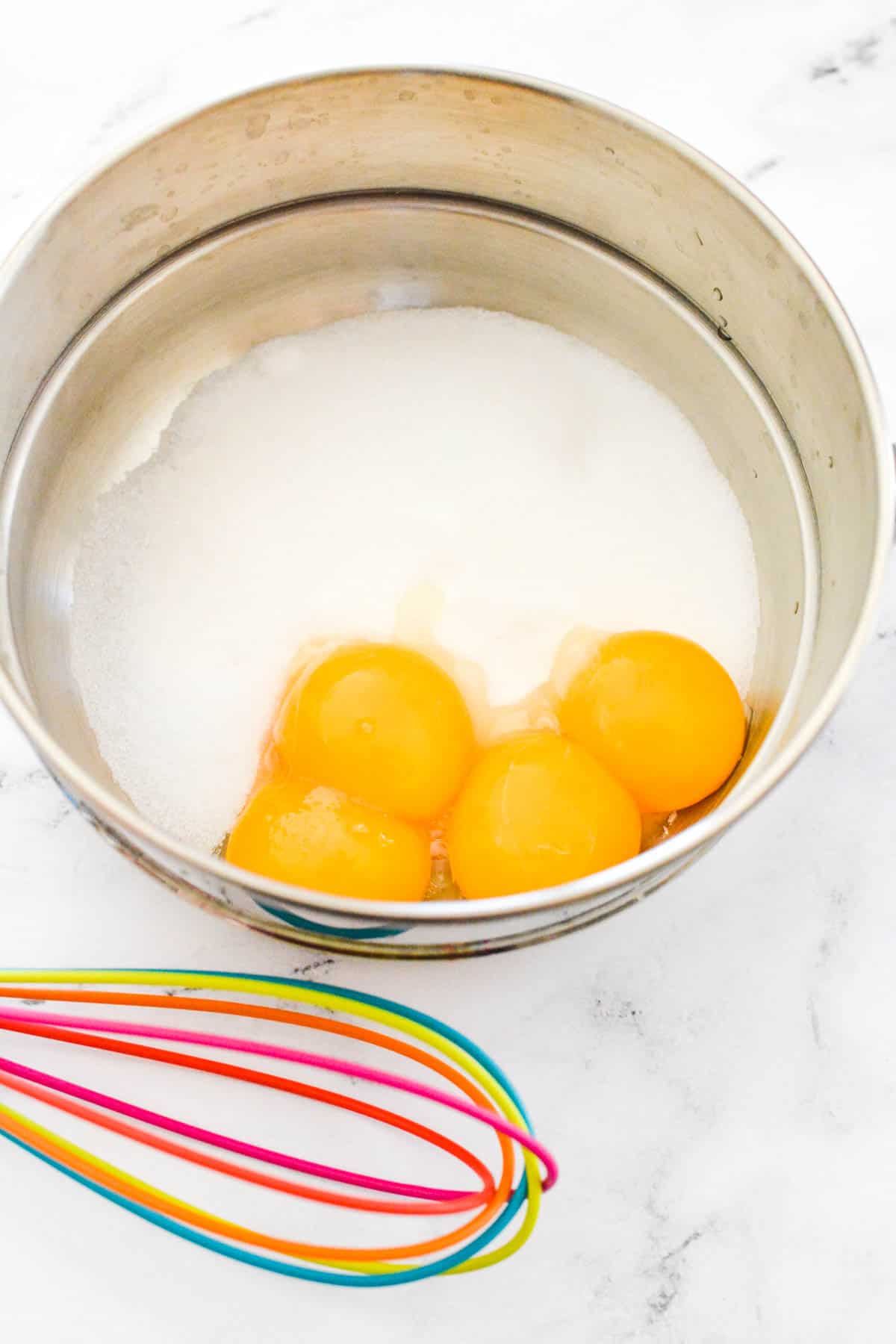 A saucepan with cream and eggs with a whisk next to it.