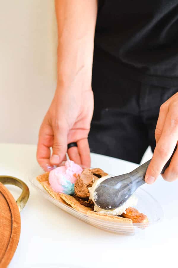 A man adding ice cream to a dish holding graham crackers and brownie brittle for a sundae.