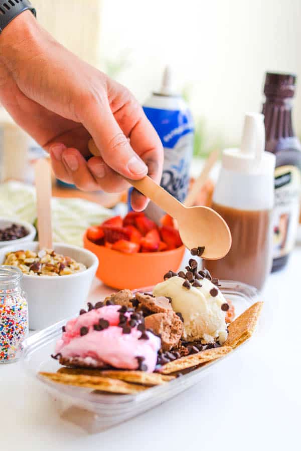 A hand adding mini chocolate chips to their ice cream nachos sundae.