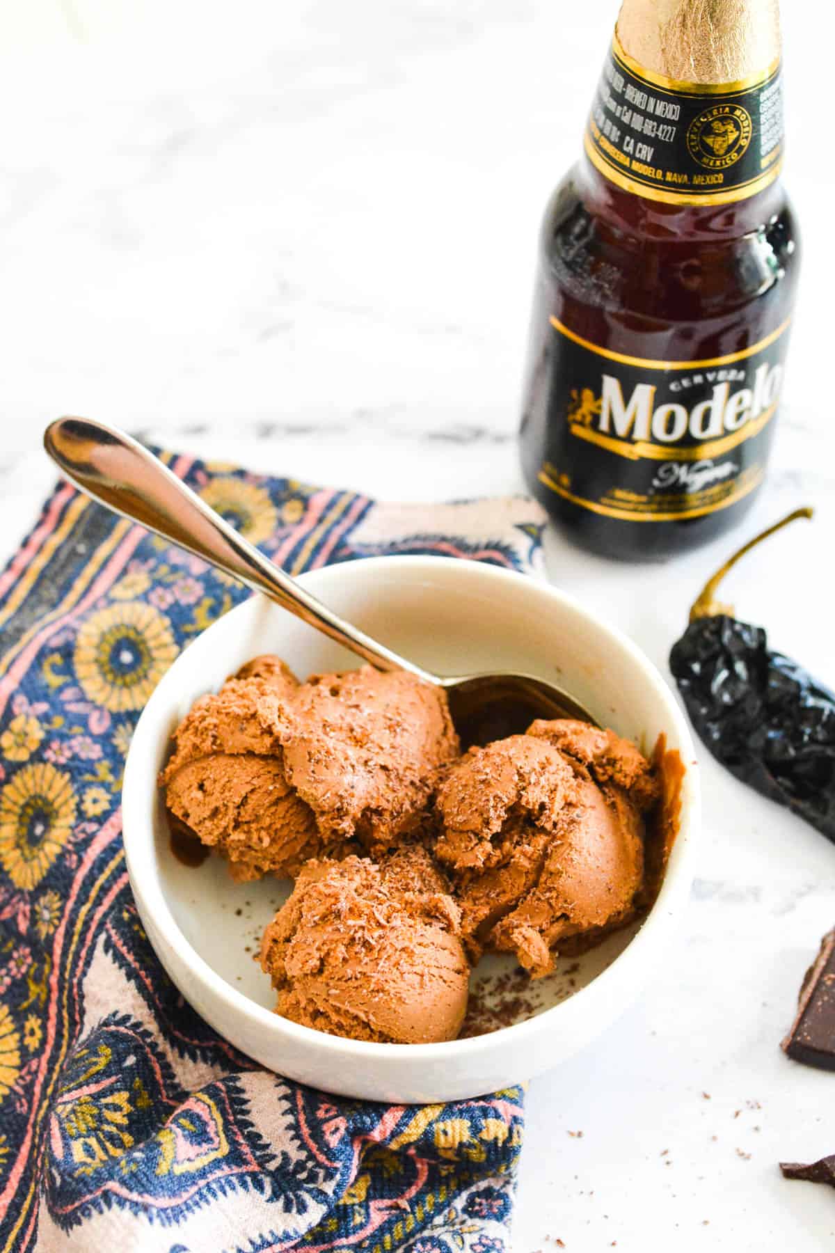 A white bowl of chocolate and beer infused ice cream with a spoon and a bottle of beer in the background.