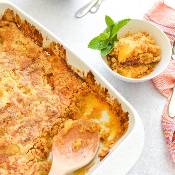 Baking dish with peach dump cake with a small plate and a portion of peach dump cake. 