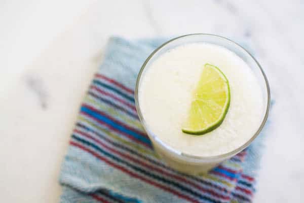 A frozen margarita with a lime wedge on top on a napkin on a table.