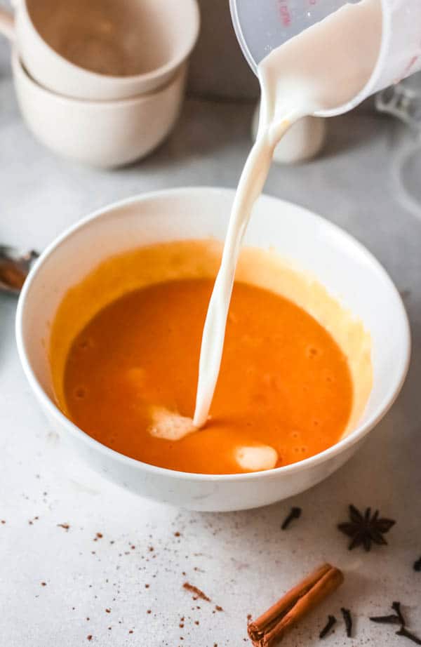 Adding milk to a bowl with a pumpkin mixture. 