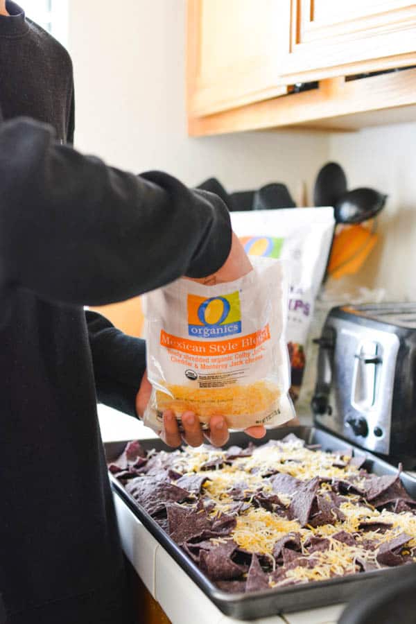 Boy putting cheese on top of nachos.