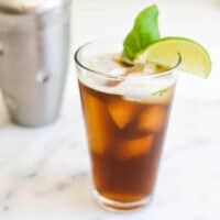 Glass of iced tea garnished with a lime wedge and fresh basil leaf with cocktail shaker in the background.