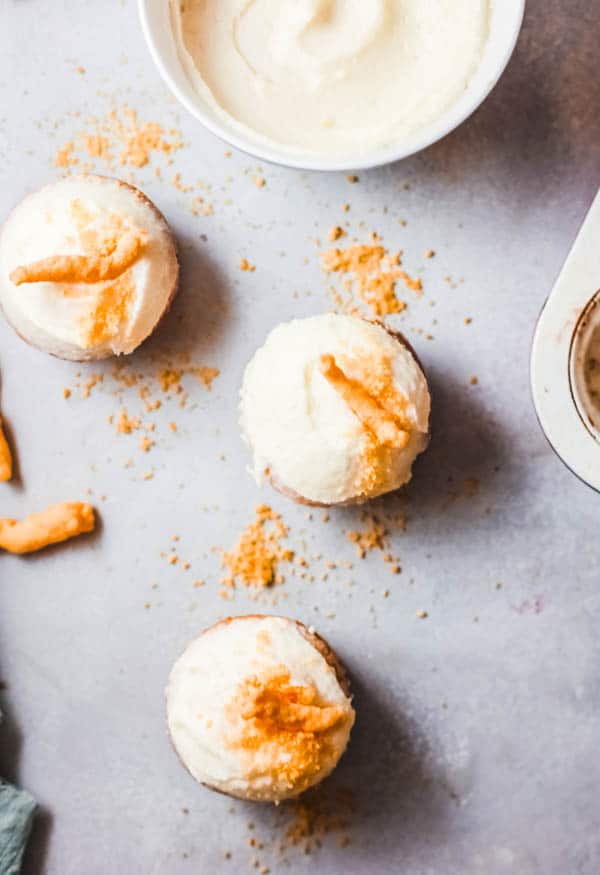 Cheeto Cupcakes on a table next to a bowl of cream cheese frosting.