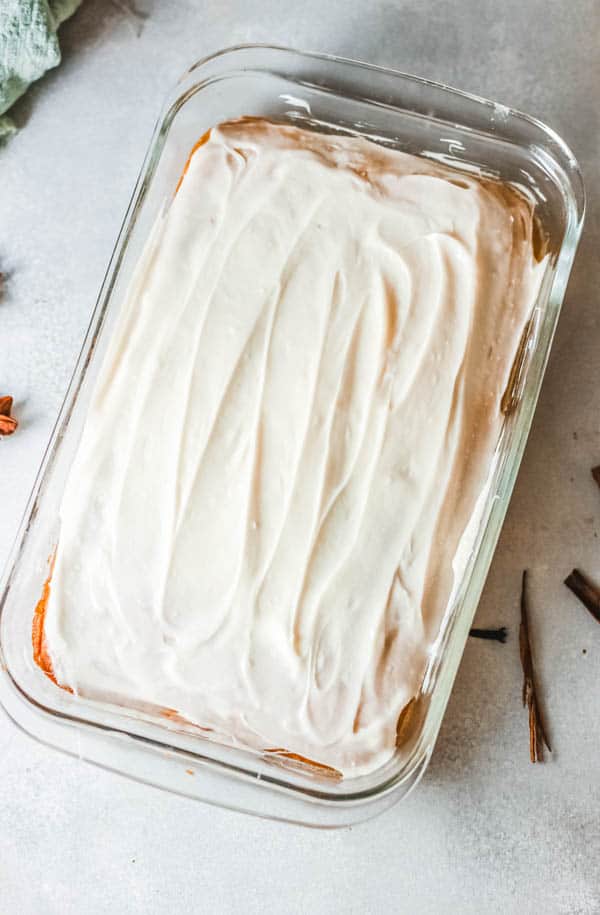 Baking dish with frosted Pumpkin Cake on a table with fresh spices around it.