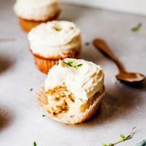 Close up of a frosted elderflower cupcake with a bite out of it on a table.