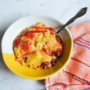 Close up of a yellow and white serving dish with cherry dump cake in it.