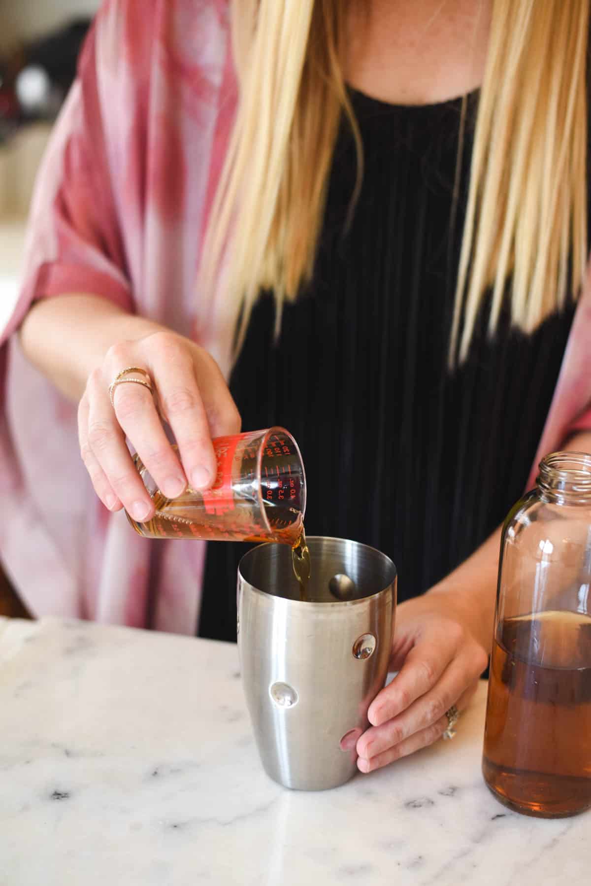 Woman adding herbal tea to a cocktail shaker.