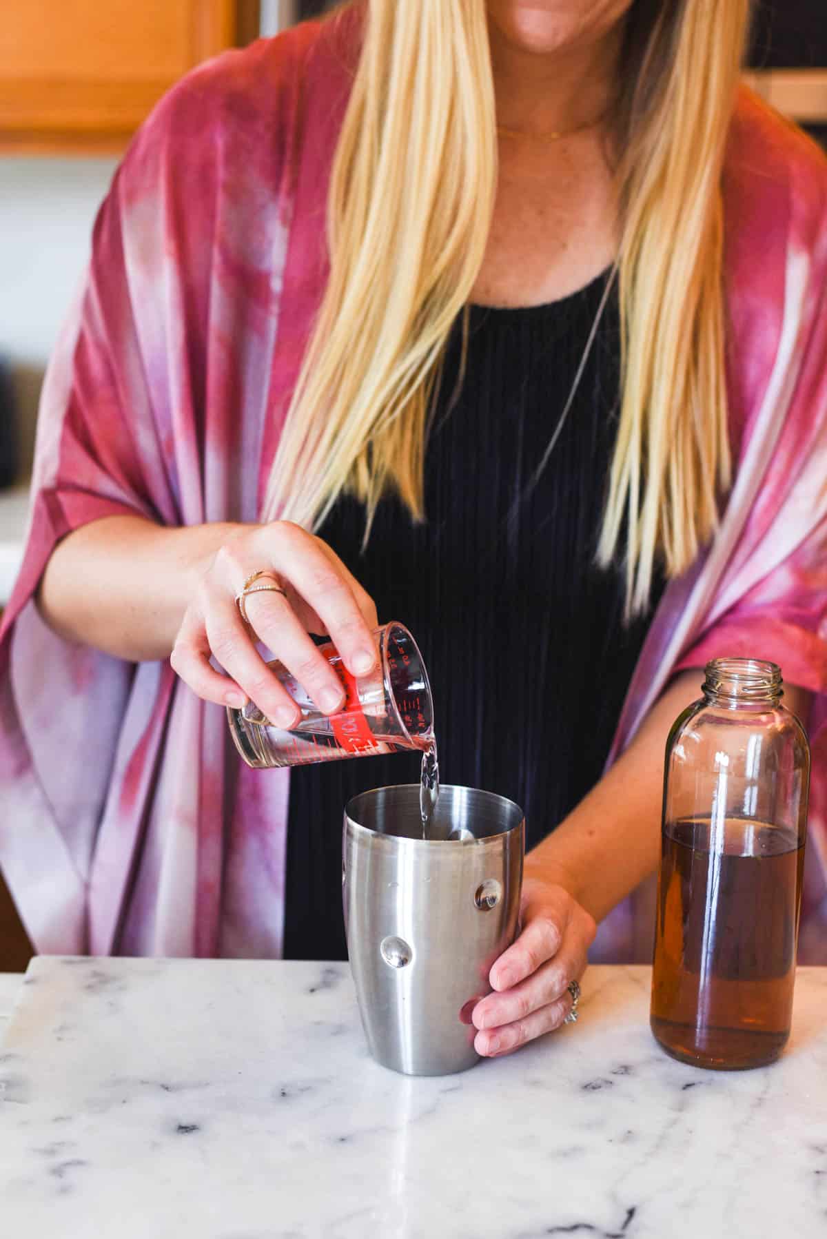 Woman adding tequila to a cocktail shaker.