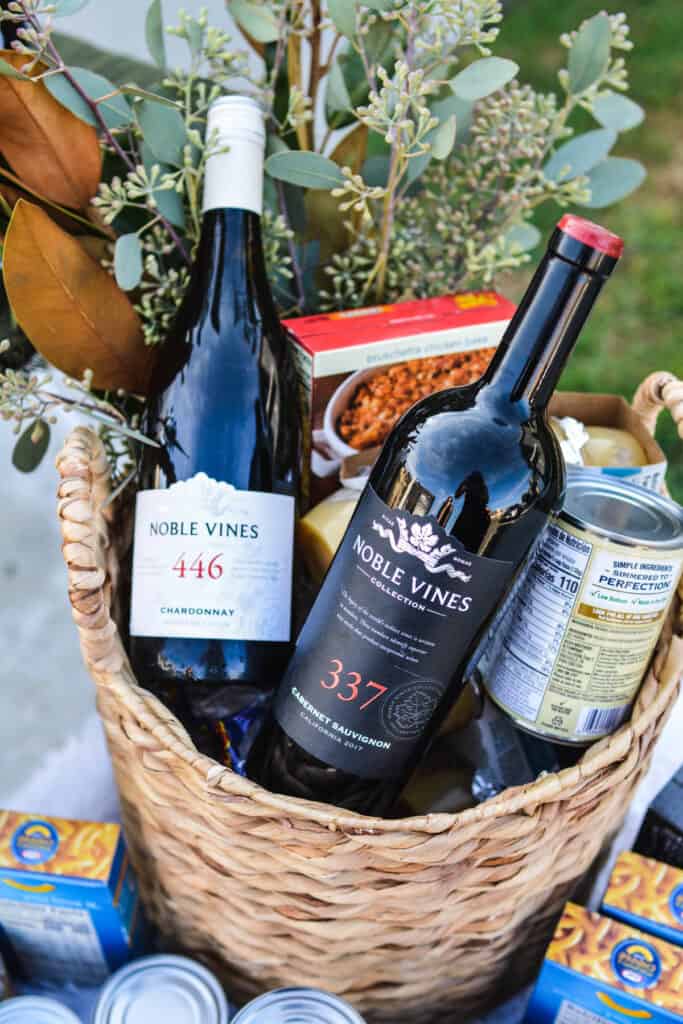 Basket holding canned goods and a bottle of red and white wine.