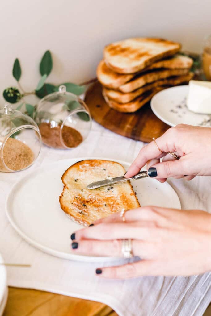 Woman spreading butter on a piece of toast on a buffet table.