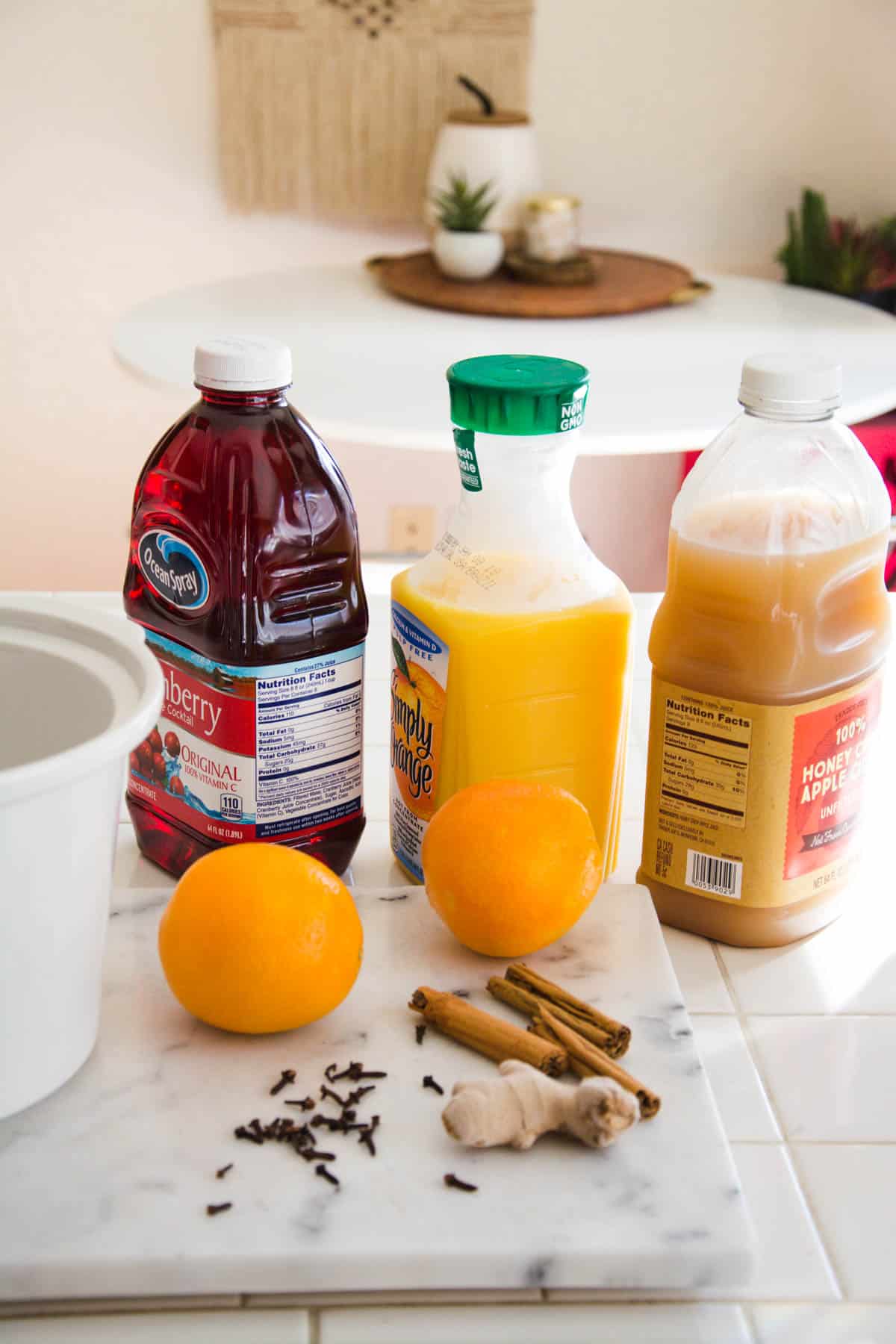 Ingredients to make slow cooker Christmas punch with cranberry juice on a counter next to a crock pot.