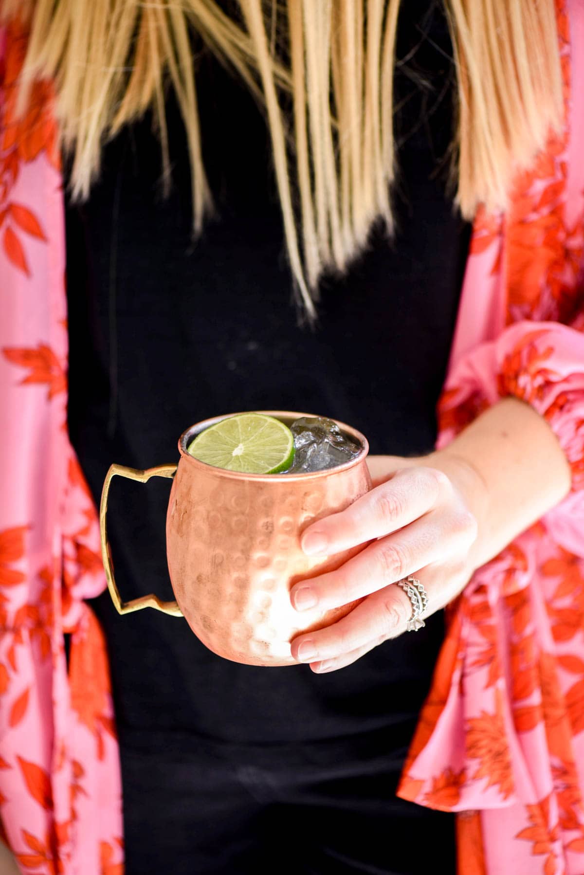 Woman holding a copper Moscow Mule mug with a cocktail and lime garnish.