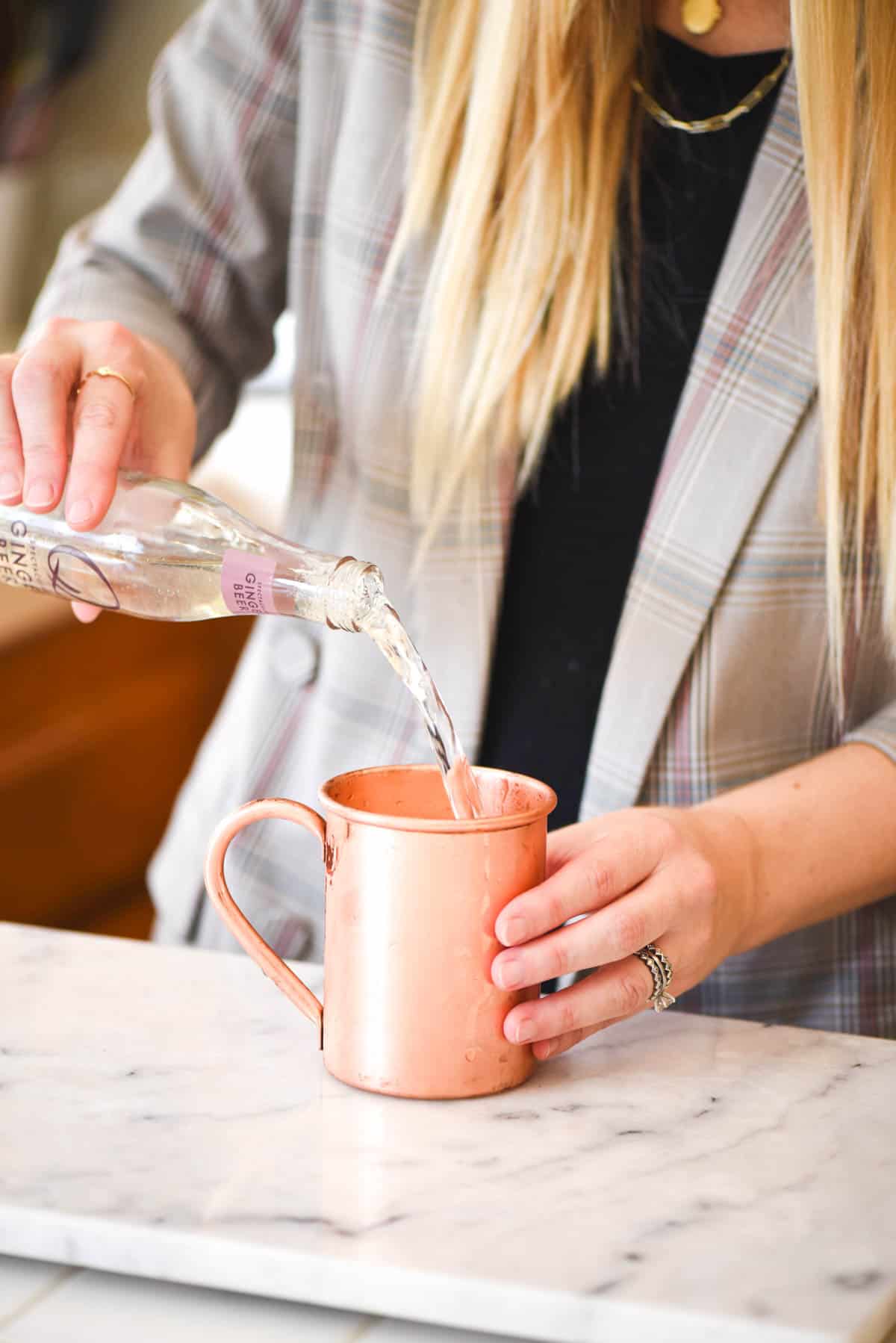 Woman adding ginger beer to a copper mule mug.