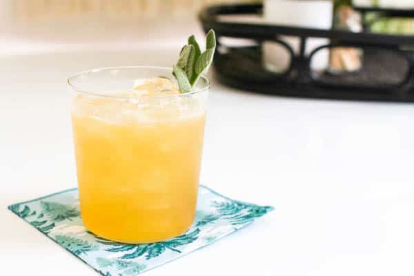 A cocktail on a napkin on a table garnished with sage.