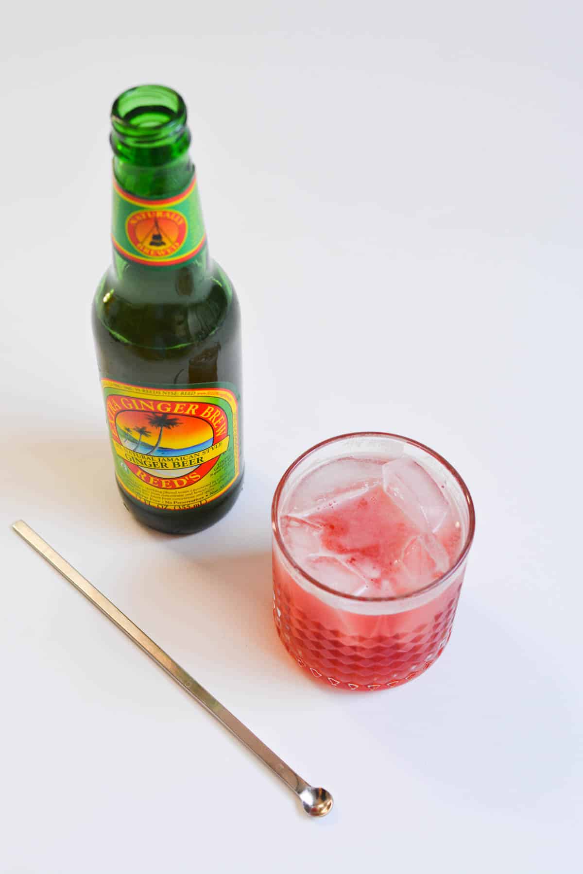 Cranberry cocktail on a table next to a bottle of ginger beer.