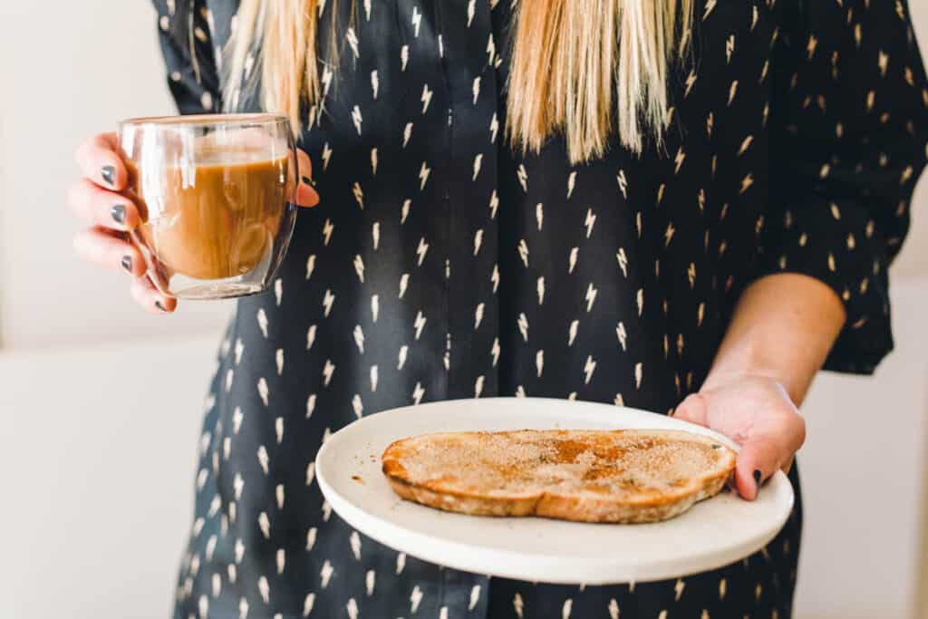 Woman holding a cup of coffee and a piece of cinnamon toast.