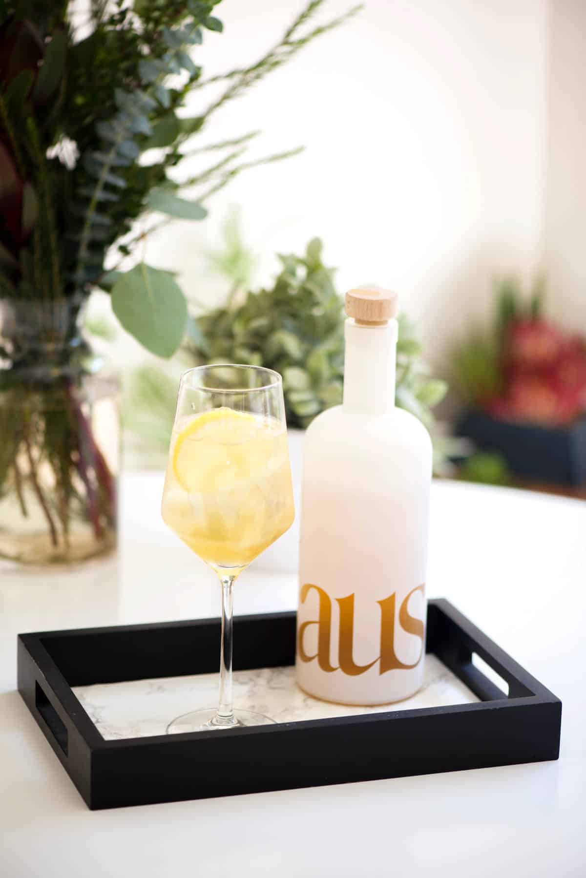 Cocktail in a wine glass next to a bottle of wine on a tray on a table.