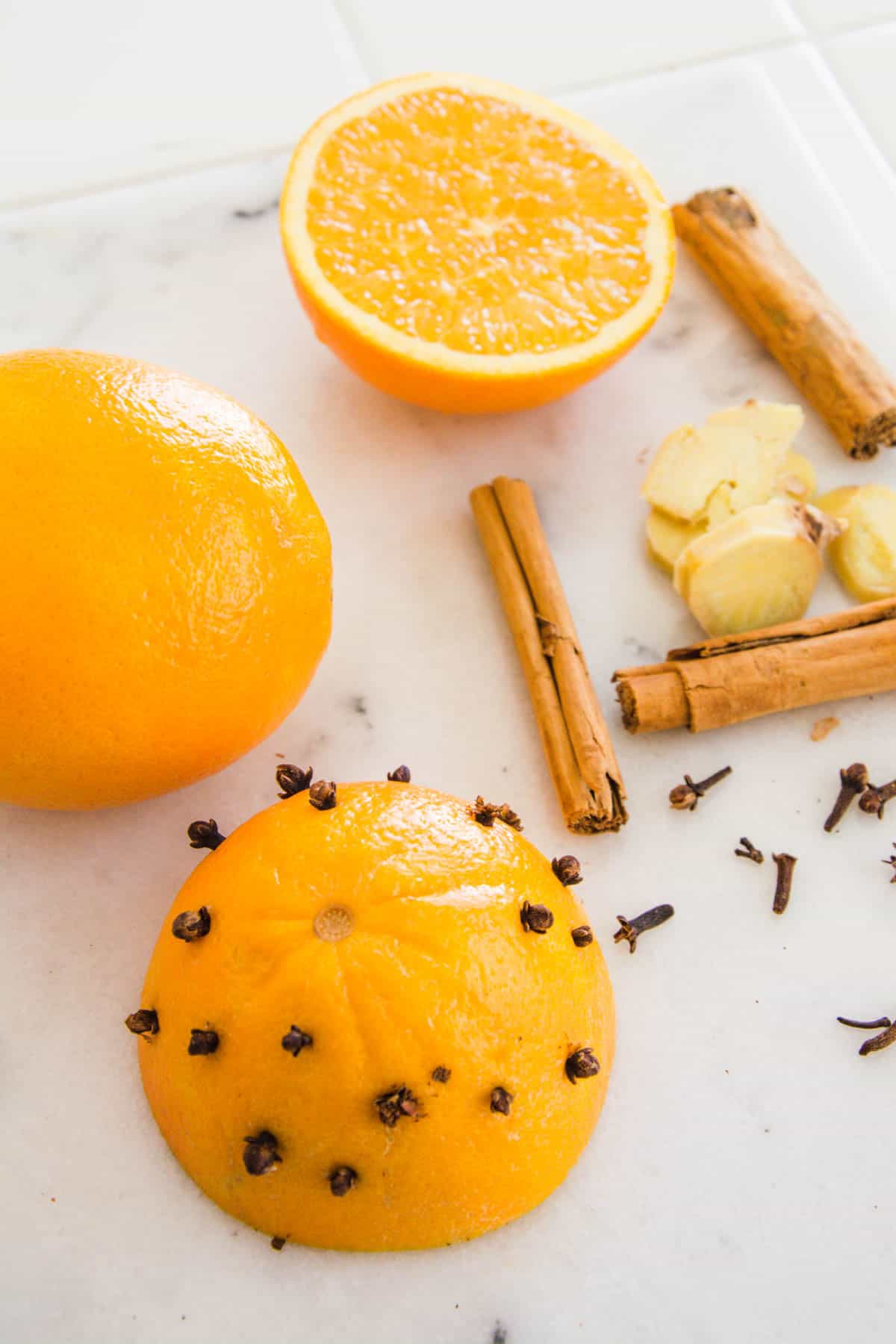 Clove studded orange on a cutting board next to whole spices of ginger and cinnamon.