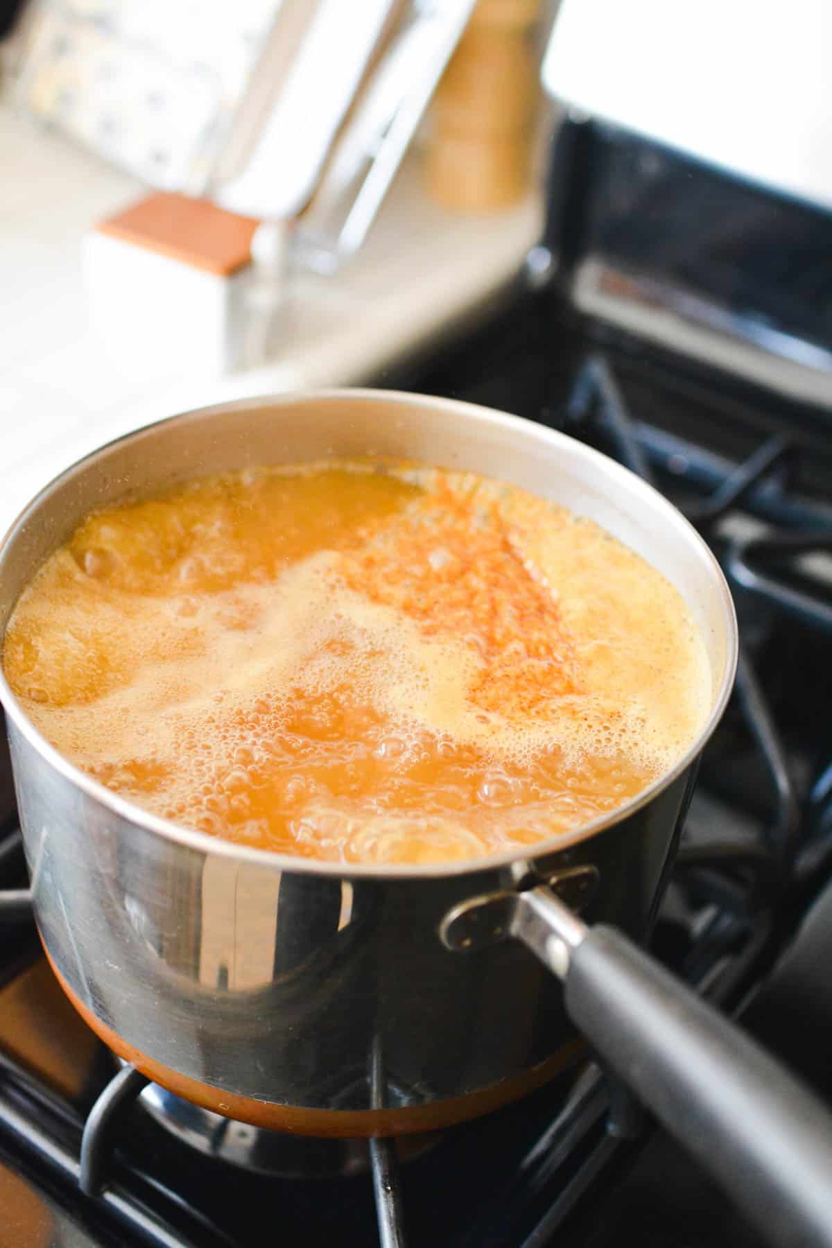 Hot apple cider boiling in a sauce pan on the stove.