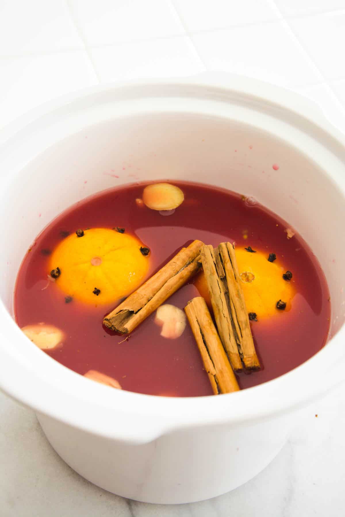 Overhead view of a slow cooker with juice, oranges and spices to make a Christmas punch.