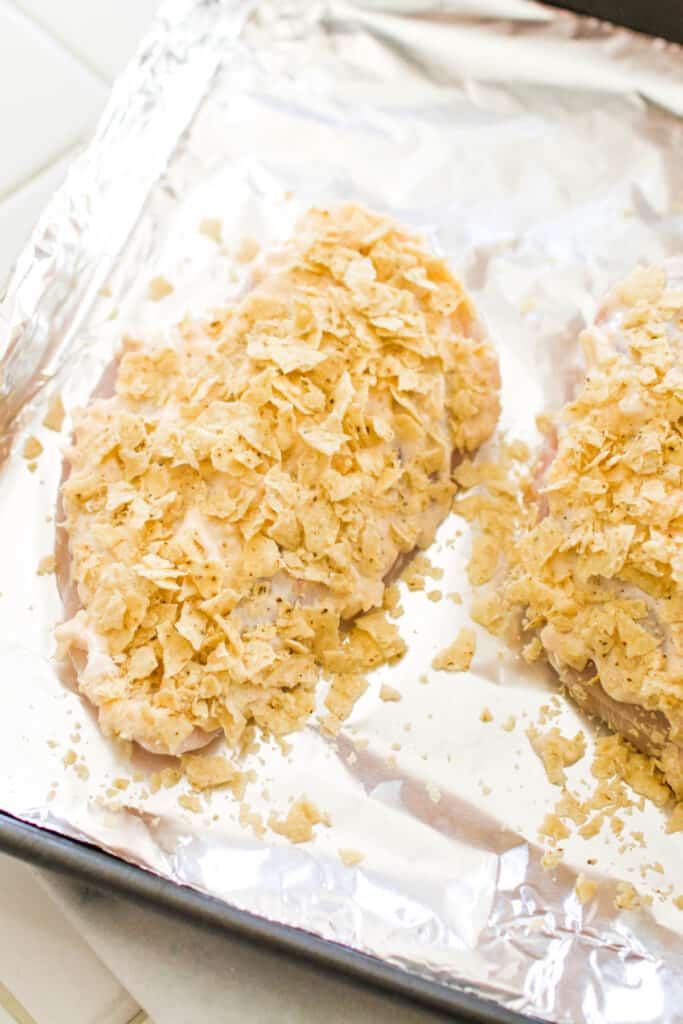 A baking sheet topped with a chicken breast coated in tortilla chips.