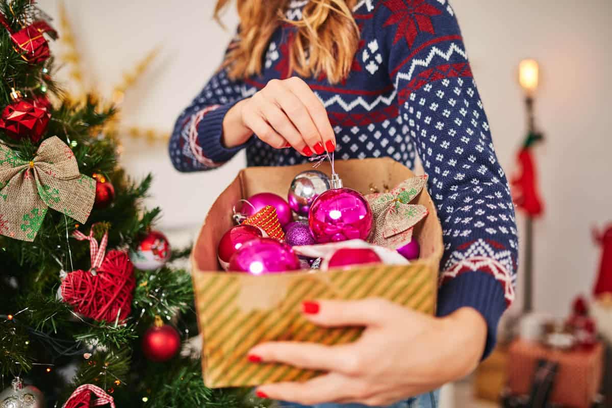 Woman taking a hot pink ornament out of a box.