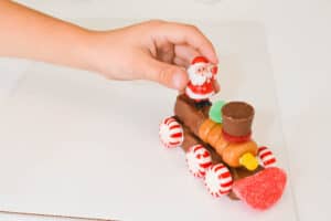 Kid putting a plastic Santa Clause miniature on the back of a candy train car.