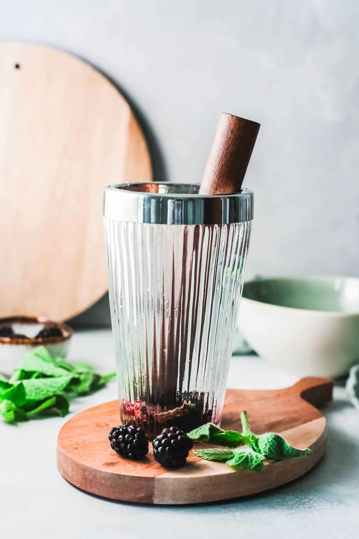 A cocktail shaker on a cutting board with a muddler sticking out.