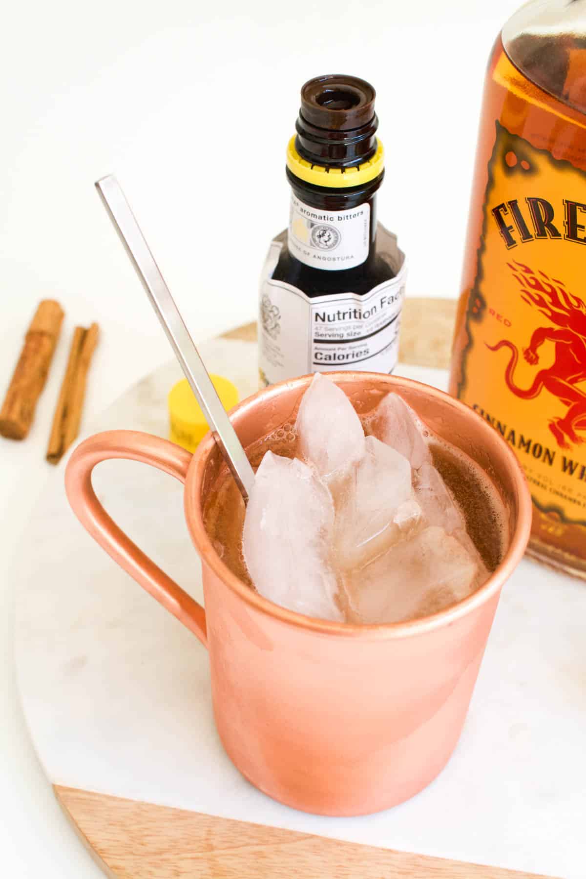 A copper mug on a table next to cocktail ingredients with a bar spoon in it.