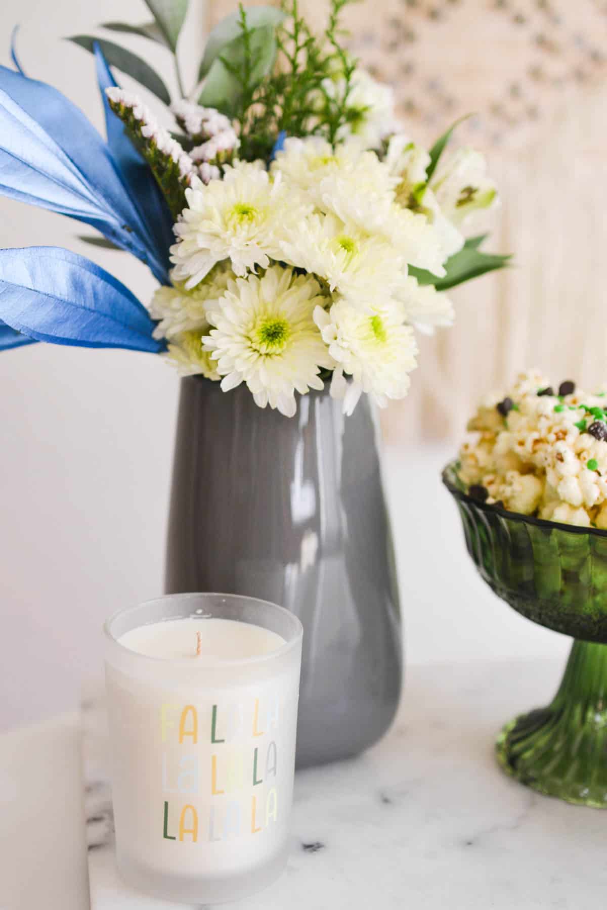 Close up of a holiday candle next to a vase of flowers.