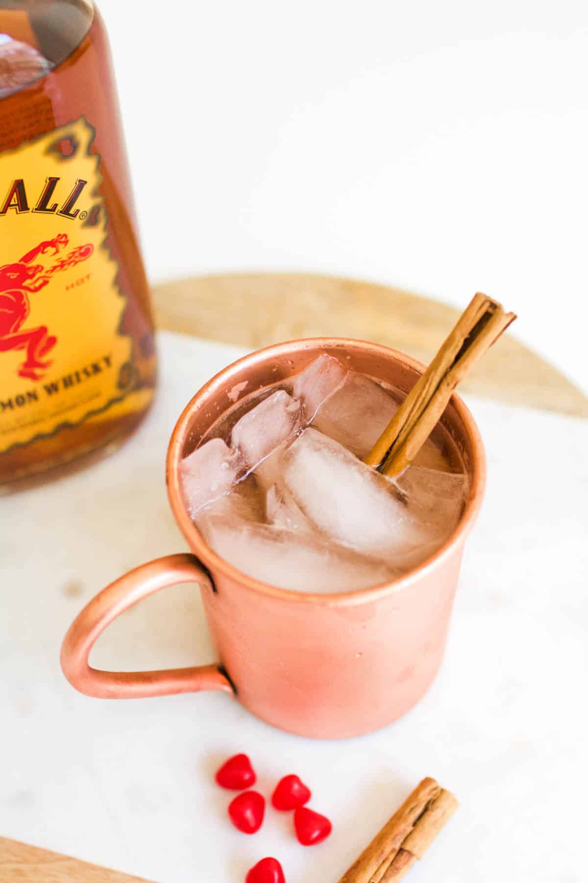 Close up of a cocktail in a copper cup on a table next to a bottle of Fireball.