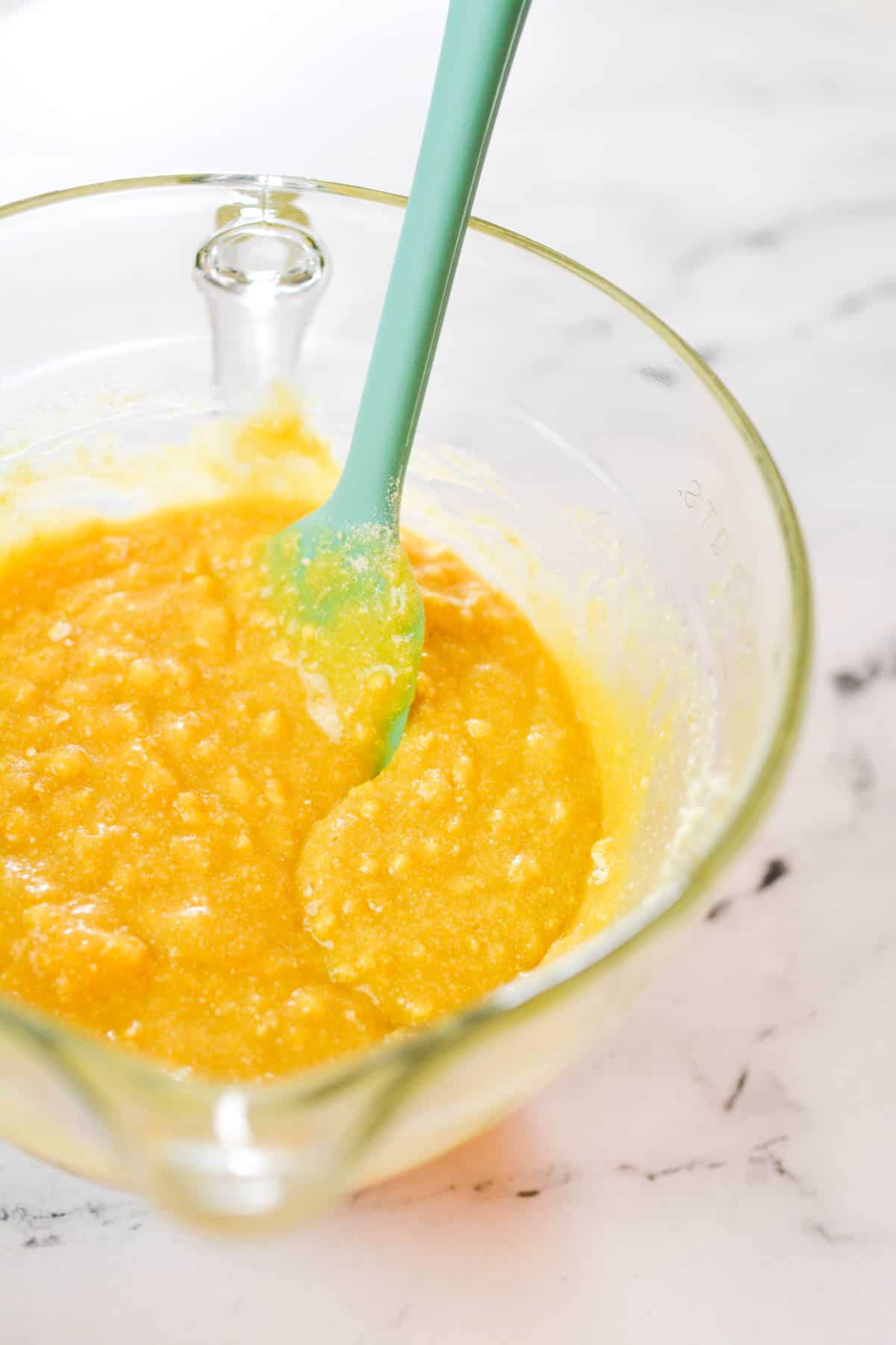 Cake batter in a mixing bowl with a spoon in it.