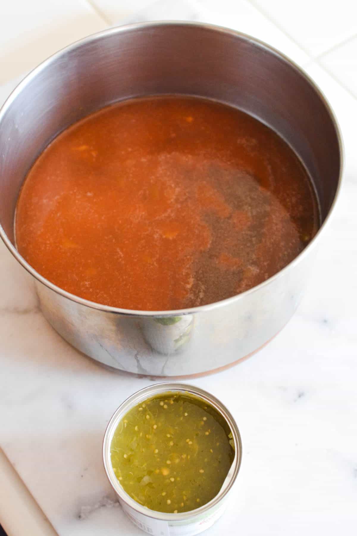 Overhead view of a pan with soup in it next to a small bowl of green salsa.