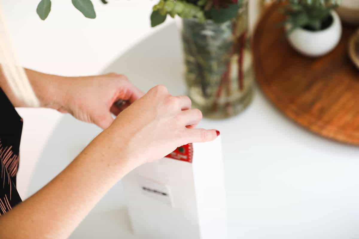 Woman adding something to the top of a paper lunch sack.